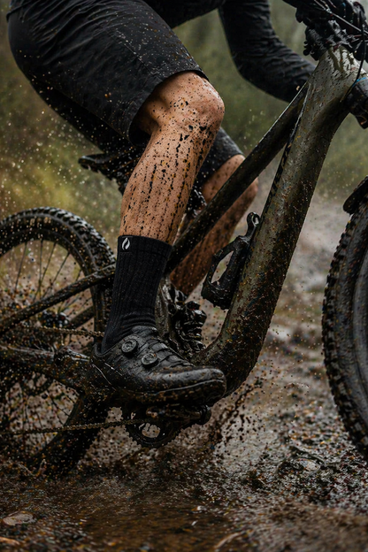 Person riding a bike through mud, with focus on the bike's suspension and muddy terrain.